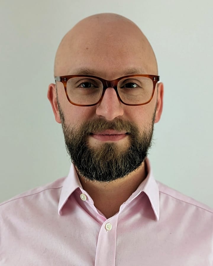 Tim, smiling, in glasses and a pale pink shirt
